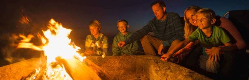 Jeunes parents et leurs trois petits garçons préparant des choco-guimauves autour d’un feu de camp.