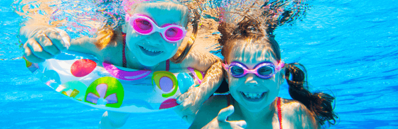 Deux fillettes portant des lunettes de protection en nageant sous l’eau.